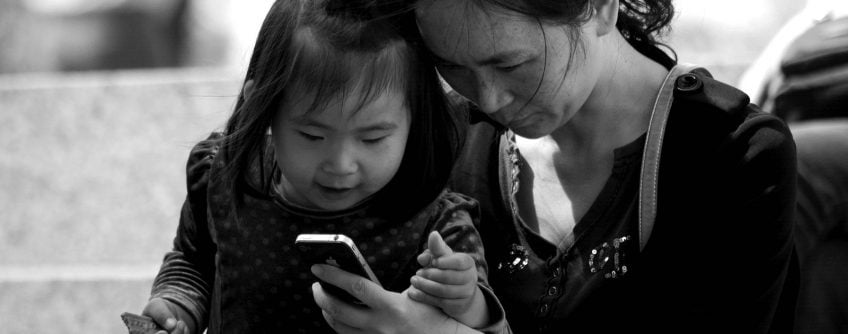 a woman is holding an iPhone in her hand, a little girl is sitting on the woman's lap, they are looking at the phone screen together