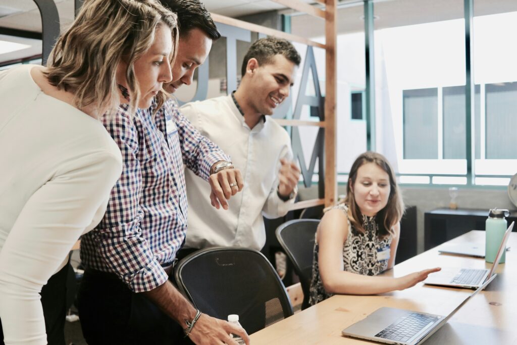 Four colleagues are looking at the laptop screen at their workspace - DevTeam.Space